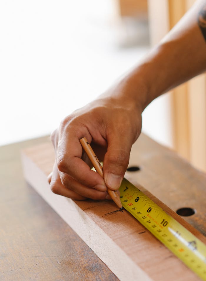 Detailed view of a craftsman using a tape measure and pencil on wood. Ideal for woodworking and craftsmanship themes.